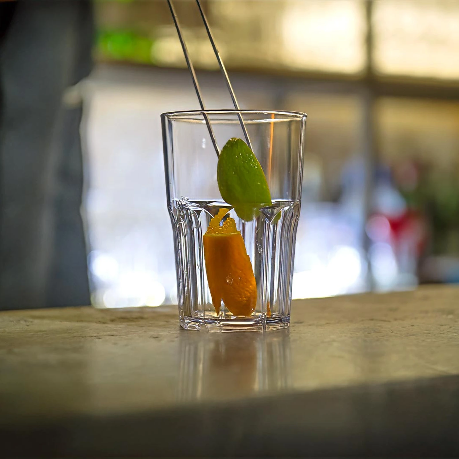 verre incassable Granity Clear 40 cl sur le comptoir, zeste d'orange et citron vert posés à la pince à garniture
