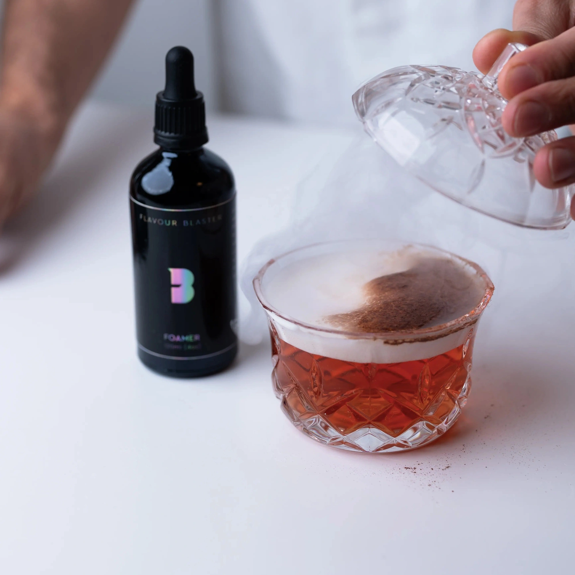 foamer cocktail Flavour Blaster : mousse sur un cocktail rouge dans un verre en cristal taillé, cloche en verre soulevée, flacon à côté